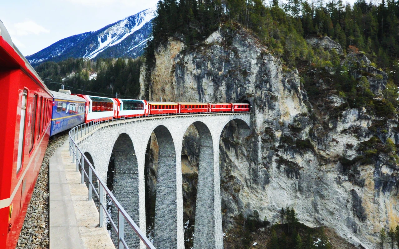 View from outside a window of a Swiss train along the route. The wagons in the front, passing already a tall bridge made of stone.