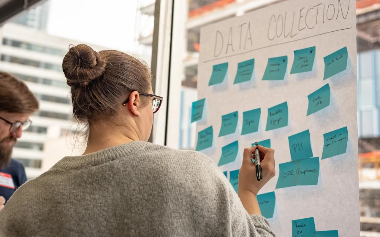 Shoulder view during workshop. Many sticky notes pasted on a board.